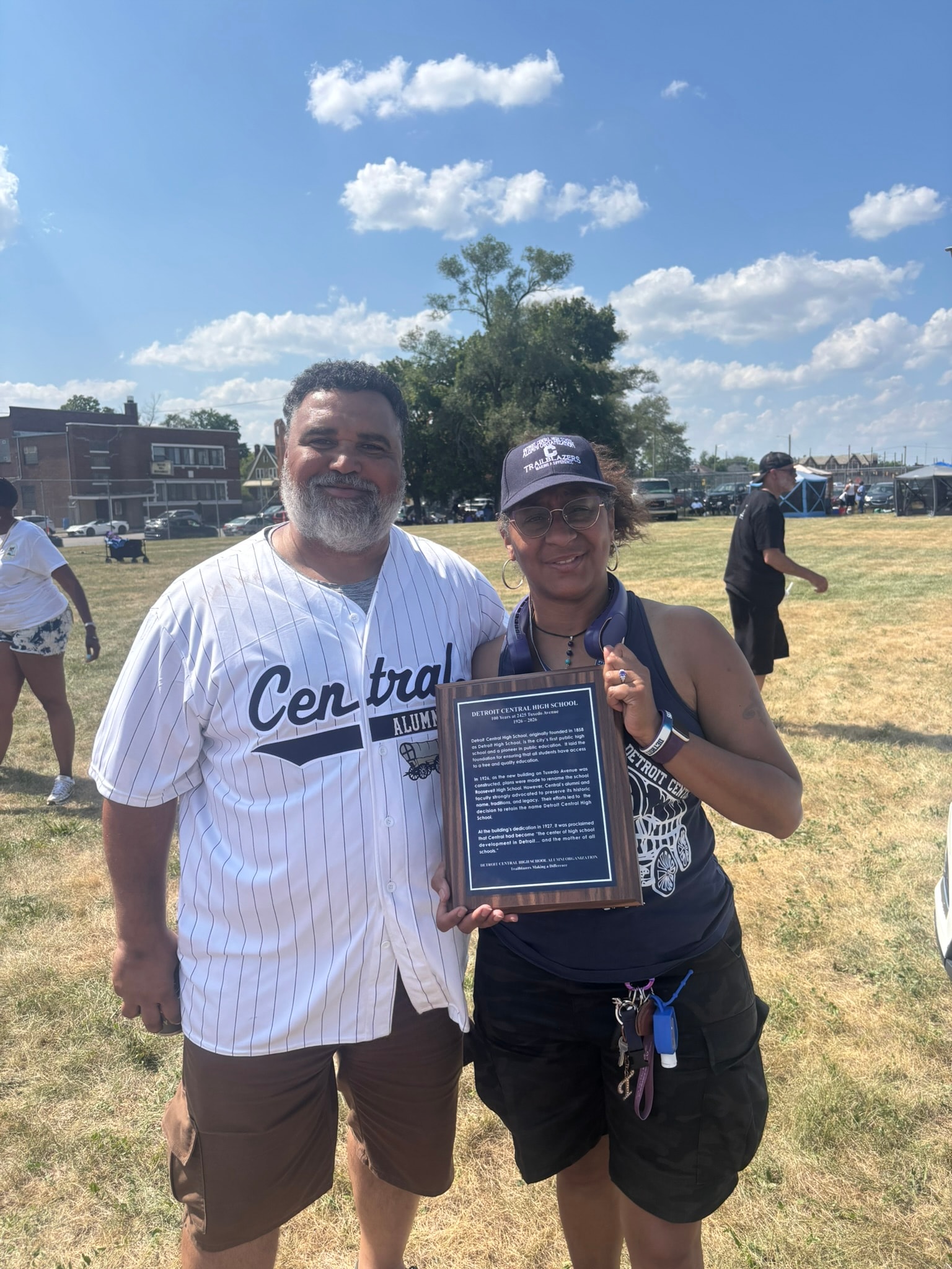 Two people holding school alumni plaque outdoors
