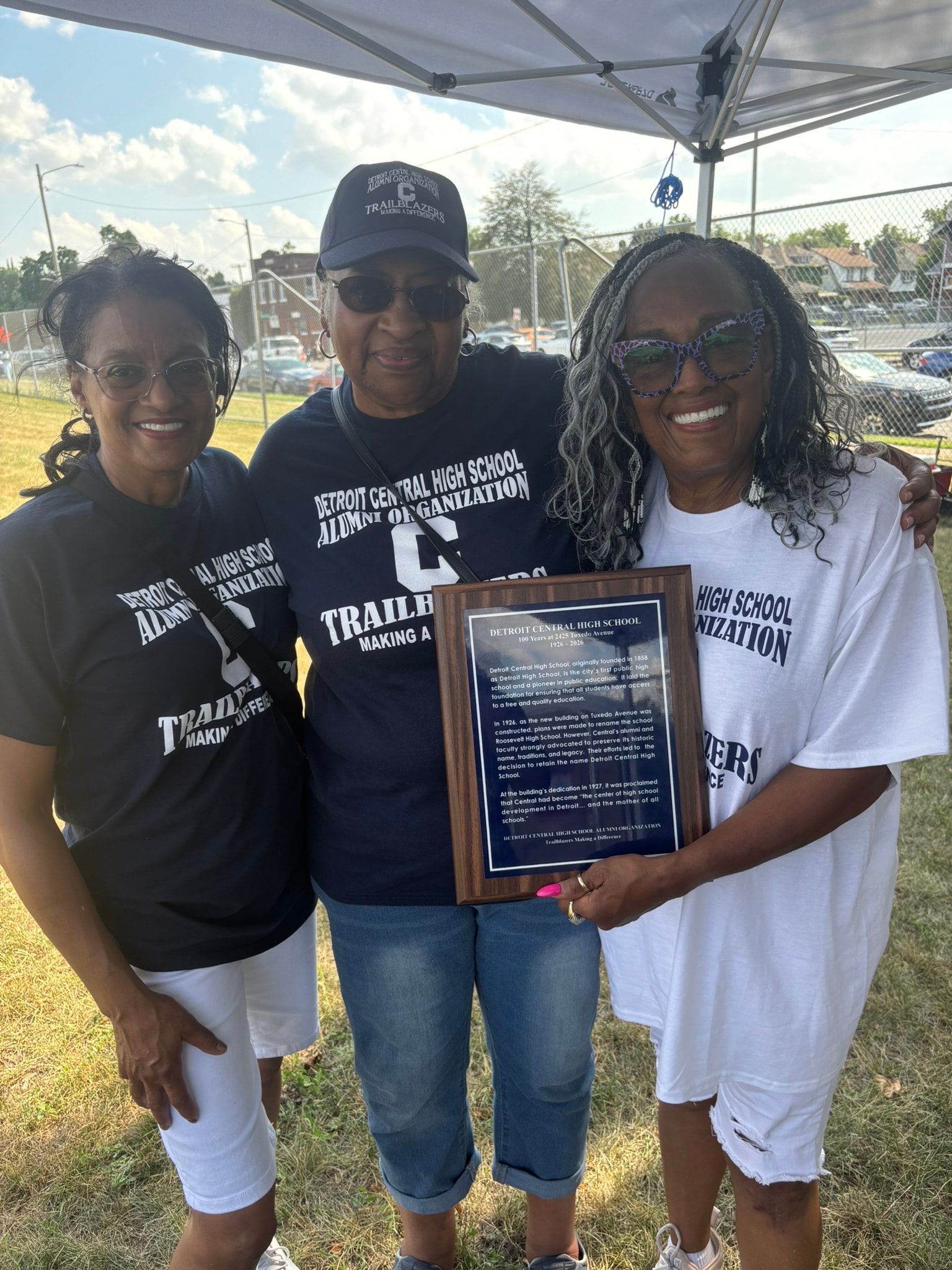 Three people holding Detroit Central High School plaque